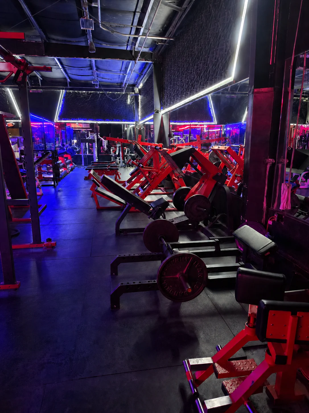 Strength training floor at Iron Arms Gym in Bakersfield with red equipment and blue and red lighting